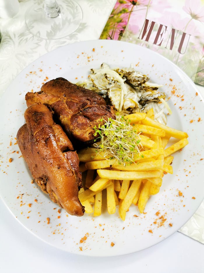 Delicious roast pork served with fries and sprouts, showcasing a culinary delight on a ceramic plate.
